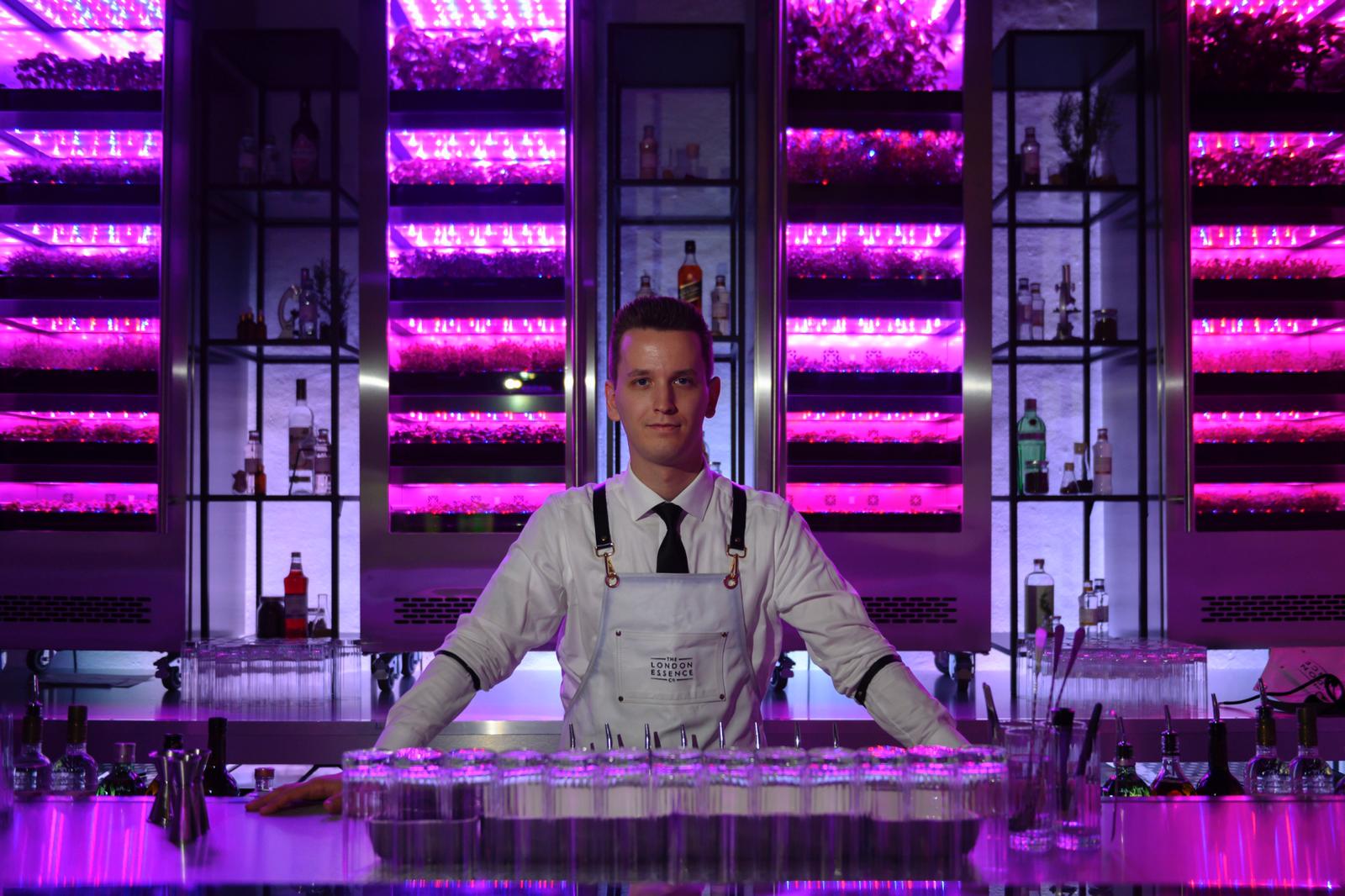 Bartender at a violet-lit London Essence botanical bar